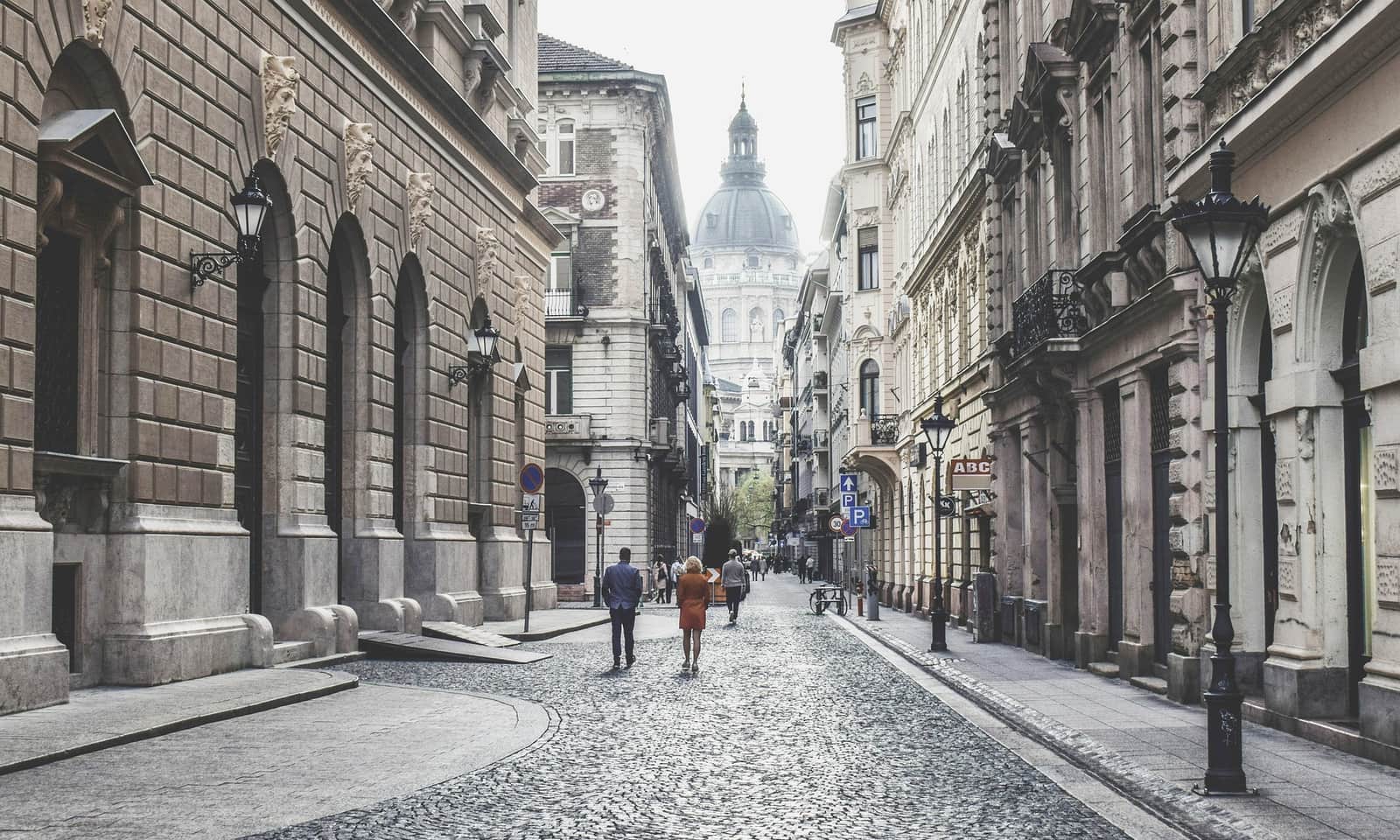 A quiet cobbled street between historic buildings, leading toward a domed basilica.